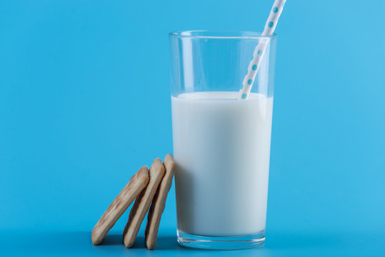 Glass of fresh cow milk with a straw and cookies on a blue background. Concept of healthy dairy products with calcium