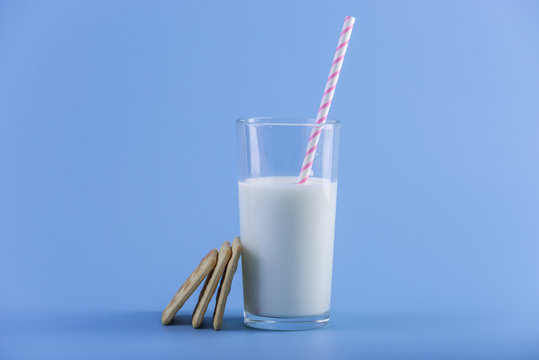 Glass of fresh milk with a straw and cookies on a blue background. Concept of healthy dairy products with calcium