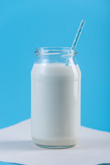 Glass bottle of fresh milk with straw on blue background. Colorful minimalism. Healthy dairy products with calcium