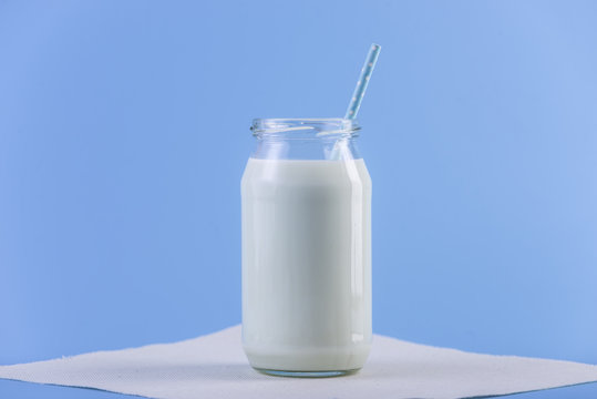 Glass bottle of fresh milk with straw on blue background. Colorful minimalism. Healthy dairy products with calcium