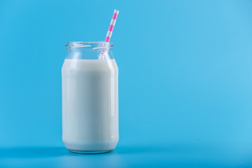 Glass bottle of fresh milk with straw on blue background. Healthy dairy products with calcium