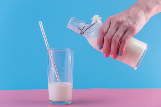 Woman's hand pours fresh milk from bottle into a glass on a pastel background. Healthy dairy products