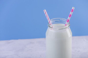 Glass bottle of fresh milk with two straws on blue background. Colorful minimalism. Healthy dairy products