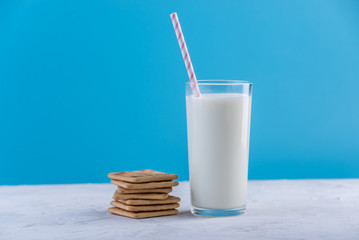 Glass of fresh milk with a straw and cookies on a blue background. Colorful minimalism. Healthy dairy products