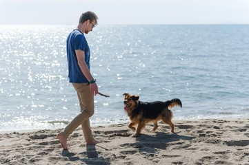 Young caucasian male playing with dog on beach. Man and dog having fun on seaside