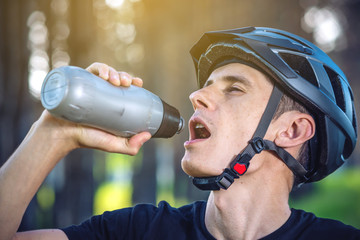 Cyclist in a helmet drinking water from a bottle while riding in the Park among the trees. Active...