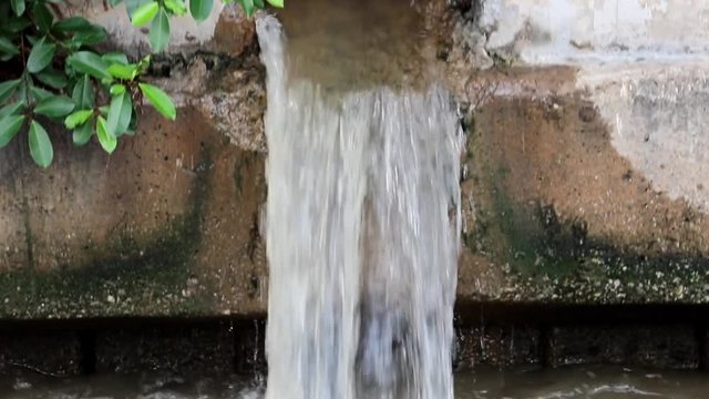 Water flows from a large hole in the wall of water canal.