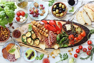Zelfklevend Fotobehang Gegrild vlees, kipspiesjes en worst met geroosterde groenten en verschillende soorten hapjes die op een buitentafel worden geserveerd. Mediterraan tafelconcept. Bovenaanzicht. © losangela