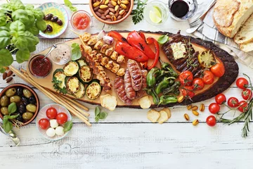 Poster Grilled meat, chicken skewers and sausage  with roasted vegetables and appetizers variety serving on party outdoor table. Mediterranean dinner table concept. Overhead view. © losangela