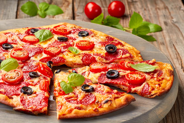 Pizza au pepperoni avec tomates cerises et olives sur table en bois