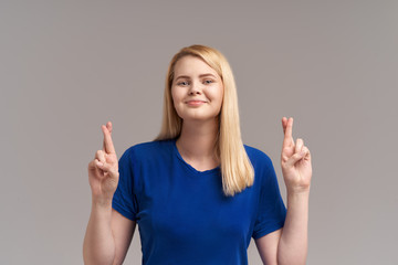 Glad beautiful young female student looks happily at camera and crosses fingers, has great desire to pass exam successfully