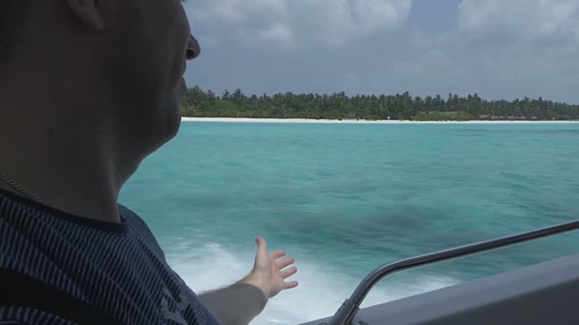 A man swims on a boat to a tropical island across the ocean, his hand slides on the water.