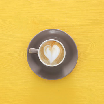 image of coffe cup with foam of heart shape over wooden yellow background.