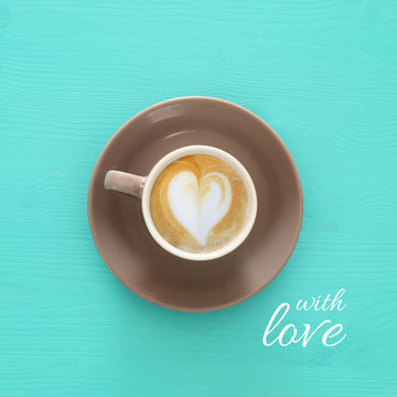 image of coffe cup with foam of heart shape over wooden blue background and text: WITH LOVE.