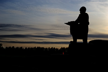 Silhouette of a child standing against the background of the evening sky over a dark forest at sunset.