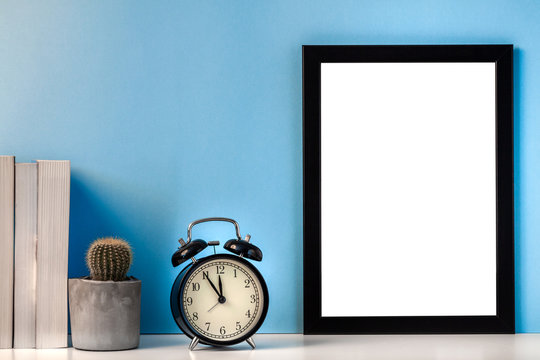 Black empty mockup frame on a blue background with a cactus, books and a black alarm clock