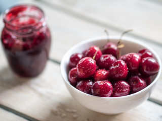 White ceramic bowl of cherries on white rustic wooden table. Close up.