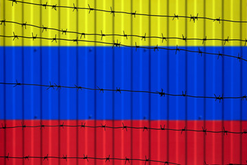 National flag of Colombia on fence. Barbed wire in the foreground symbolizes entry ban or prohibition for crossing border of country