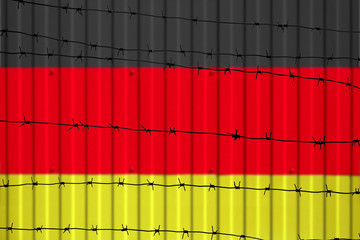 National flag of Germany on fence. Barbed wire in the foreground symbolizes entry ban or...