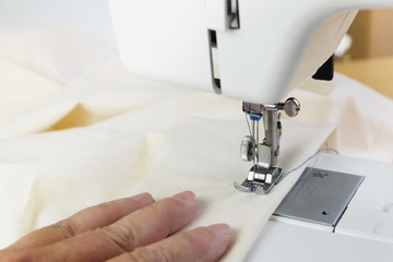sewing yourself with a hobby sewing machine, hand leads the white fabric under the presser foot, close up with copy space