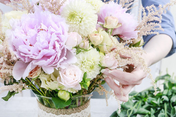Florist at work: woman arranging bouquet with pink peonies, roses and yellow dahlias