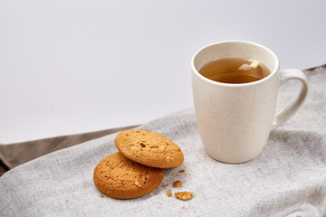 White porcelain mug of tea and sweet cookies on homespun napkin over white background, top view, selective focus