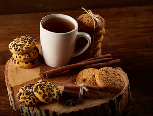 Christmas concept with a cup of hot tea, cookies and decorations on a log over wooden background, selective focus