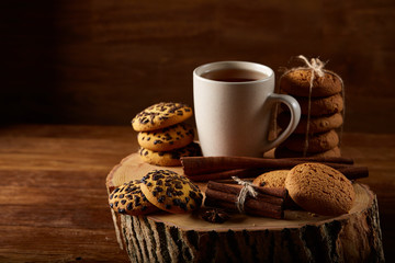 Christmas concept with a cup of hot tea, cookies and decorations on a log over wooden background, selective focus