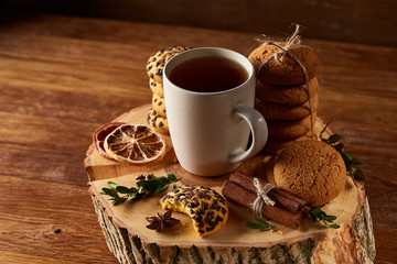 Christmas concept with a cup of hot tea, cookies and decorations on a log over wooden background, selective focus
