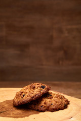 Bunch of chocolate biscuits on a round wood log over rustic wooden background, close-up, selective focus.