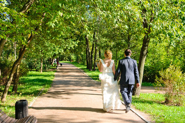 Fototapeta premium Newlyweds walk along the trees alley in the park. Wedding day in summer.