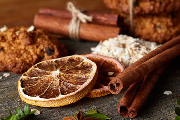 Christmas composition with chocolate biscuits, cinnamon and dried oranges on wooden background, close-up.