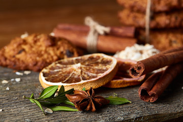 Christmas composition with chocolate biscuits, cinnamon and dried oranges on wooden background, close-up.