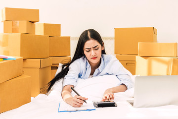 Young woman freelancer working and checklist and writing order with cardboard box on bed at home - SME business online and delivery concept