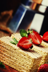 Traditional russian honey cake decorated with strawberries and green mint, old wooden background, selective focus