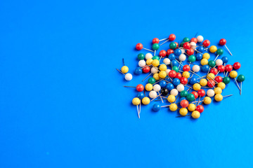Office supplies in the form of colored buttons and paper clips on blue background.