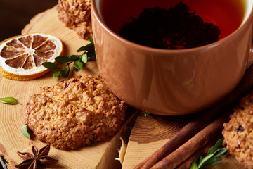 Christmas concept with a cup of hot tea, cookies and decorations on a log over wooden background, selective focus