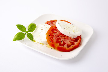 Mozzarella and tomatoes with basil on a white square plate. The background is white. Copiespice.