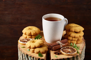 Christmas concept with a cup of hot tea, cookies and decorations on a log over wooden background, selective focus
