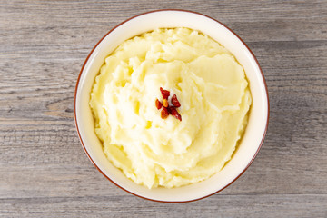 Puree from potatoes in a plate. Red pepper in the middle. Wooden background. Macro.