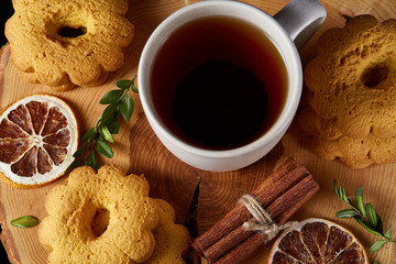 Christmas concept with a cup of hot tea, cookies and decorations on a log over wooden background, selective focus