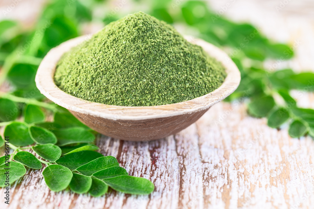 Wall mural moringa powder in coconut bowl with original fresh moringa leaves