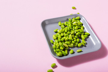 Green raw soya beans on gray square plate on pink background. Healthy food concept with coppy space.
