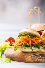 Homemade mini burgers with ham, tomato, carrot, fresh salad served on wooden board. Healthy junk food concept with copy space.