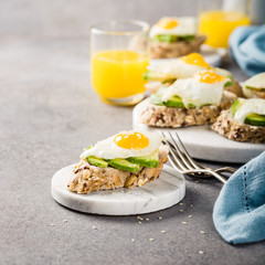 Healthy breakfast with open sandwich with fresh avocado and fried quail egg on small marble board on gray background. Copy space.