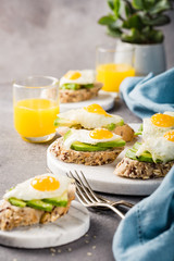 Healthy sandwich with fresh avocado and fried quail egg on small marble board on gray background. Breakfast or lunch food concept with copy space.