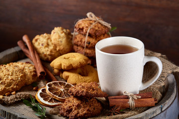 Conceptual festive composition with a cup of hot tea, cookies and spicies on a wooden barrel, selective focus, close-up