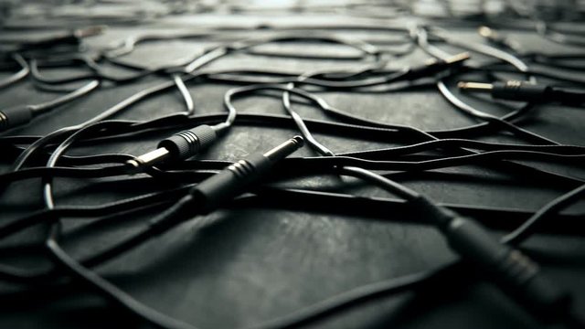 Bunch of tangled black audio cables with jack plugs lying on grey studio floor.