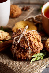 Christmas concept with a cup of hot tea, cookies and decorations on a log over wooden background, selective focus