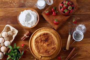 Delicious cake with fresh organic strawberries and kitchen utensils, top view, close-up, selctive focus.